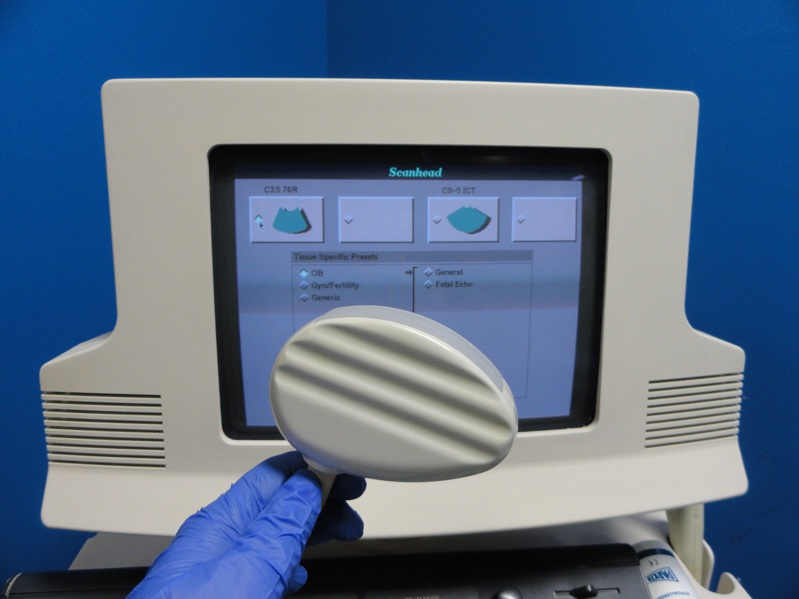 a hand in a glove touching probe in front of ultrasound